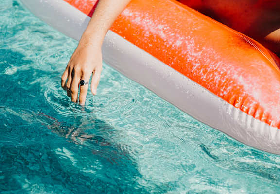 A person is floating on an orange and white float in a blue pool.