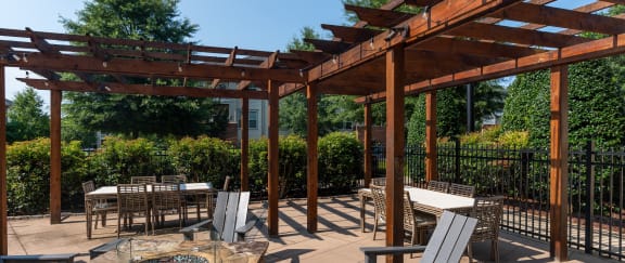 a fire pit with tables and chairs under a wooden pergola
