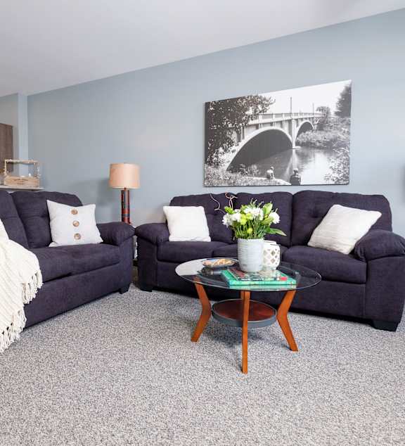 A yellow mug sits on a coffee table in front of a grey couch with a yellow pillow and a white blanket.