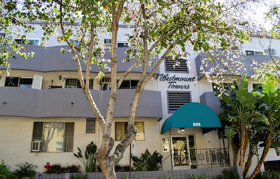 A building with a green awning and the sign "Westmount Towers 866" is surrounded by trees and plants.