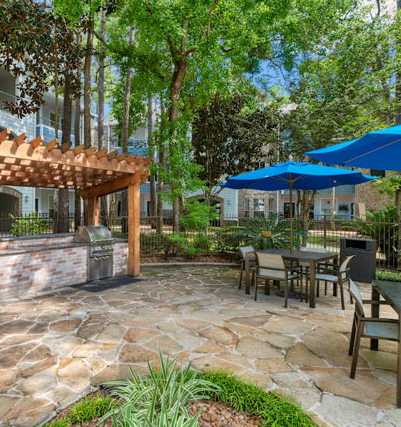 A patio with a grill and chairs under a pergola.