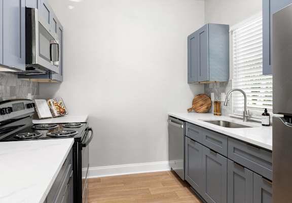 a kitchen with gray cabinets and white countertops and a stainless steel stove and sink