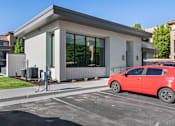 Thumbnail 20 of 28 - A red car is parked in front of a modern building with a charging station. at Siena Villas Apartments, Utah