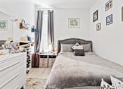 Thumbnail 7 of 24 - A bedroom with a large bed and a white dresser.