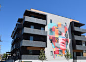 Thumbnail 1 of 8 - A large mural of a woman's face is on the side of a modern building.