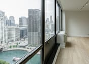 Thumbnail 7 of 8 - A room with a large window overlooking a river and city buildings.