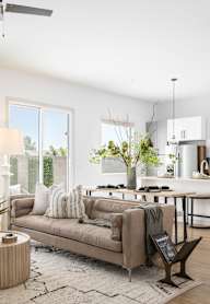 A well-lit, modern living room with a large sofa, a coffee table, and a kitchen area in the background.