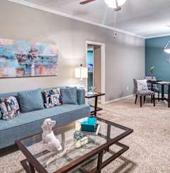 A living room with a grey couch, a glass coffee table, and a painting on the wall at Austin Chase Apartments, Macon, GA
