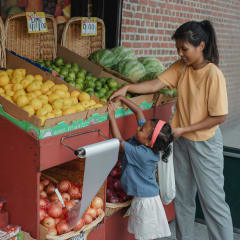 a woman and a child buying fruit at a fruit stand