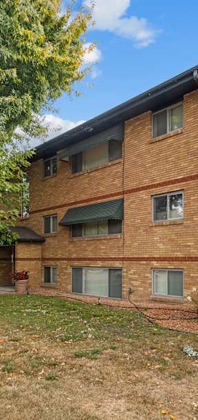A multi-story apartment building with a brick facade and a tree with yellow leaves in front.