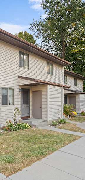 A beige two-story apartment building with a brown roof and a small front yard.