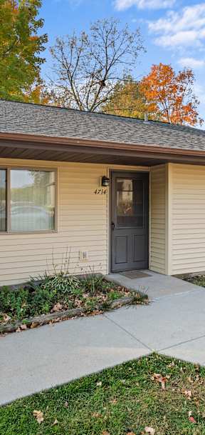 A small house with a brown roof and a grey siding with a black door and a small window.