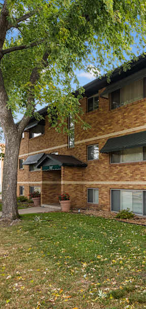 A brown and white apartment building with a tree in front.