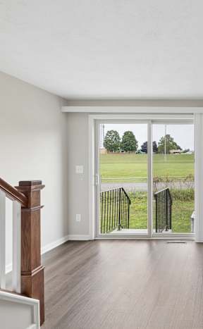 A room with a wooden floor and a sliding glass door leading to a green lawn.