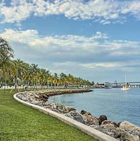 A pathway runs along a grassy area next to a body of water with a boat in the distance.