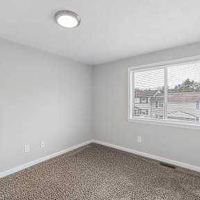A room with a carpeted floor and a window showing a view of a residential area.