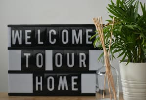 A vase with a green plant next to a sign that says, "Welcome to Our Home."