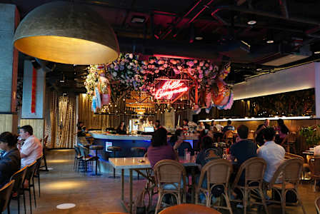 A restaurant with people sitting at tables and a neon sign that says "Happy Hour".