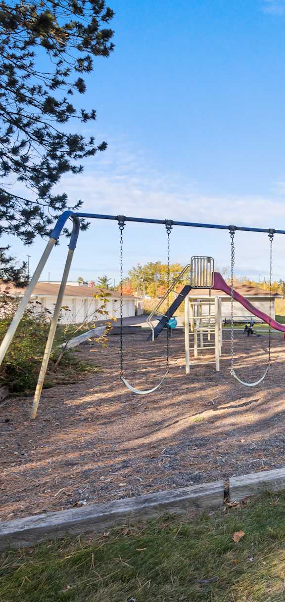 A playground with a swing set and a building in the background.