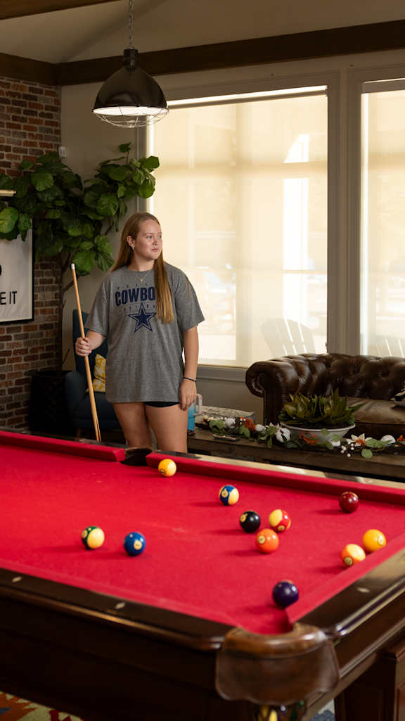 a red pool table in a living room with a brick wall at Midtown Sam Houston Apartments, Huntsville, TX, 77340