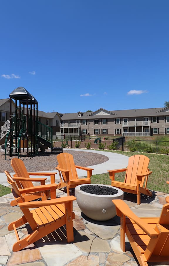 A playground with a slide and a fire pit surrounded by chairs.