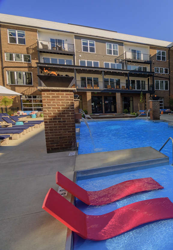 an outdoor pool with red chairs and an apartment building