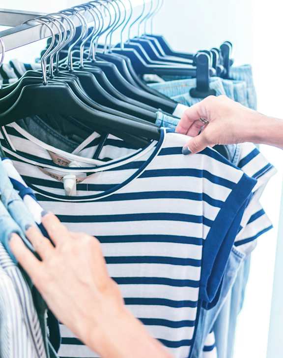 A person is holding a striped shirt in front of a rack of clothes.