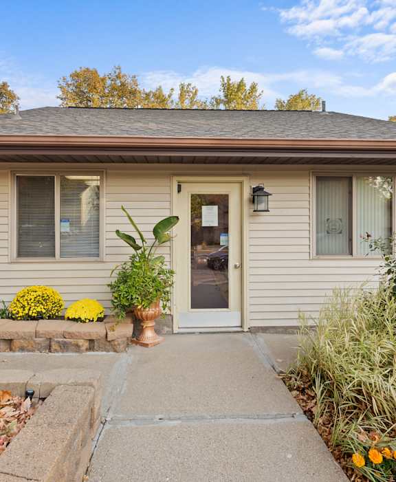 A house with a brown roof and a grey door surrounded by plants and flowers.