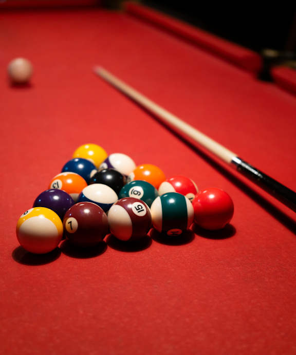 A pool table with a pyramid of balls and a cue stick.