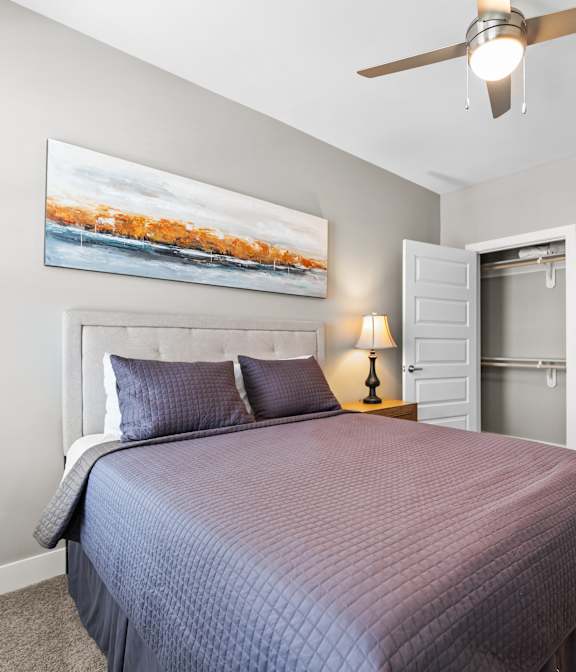 A bedroom with a bed, a ceiling fan, and a painting on the wall.