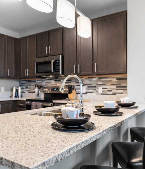 A modern kitchen with a granite countertop and black chairs.