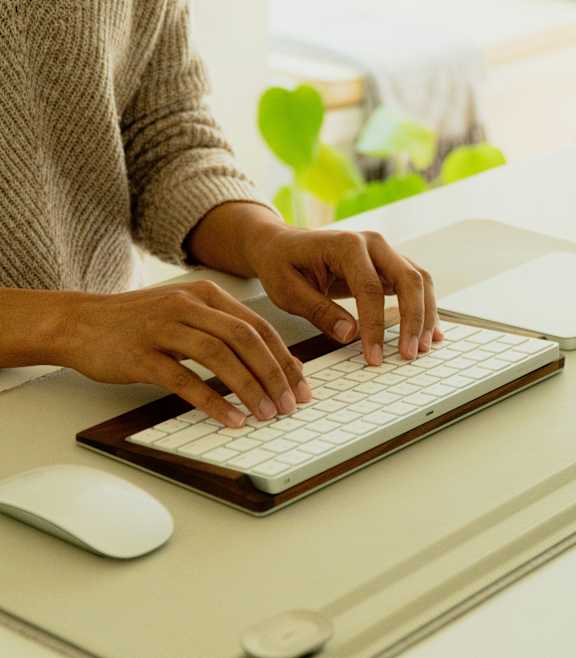 A person is typing on a keyboard with a mouse and a notepad beside them.