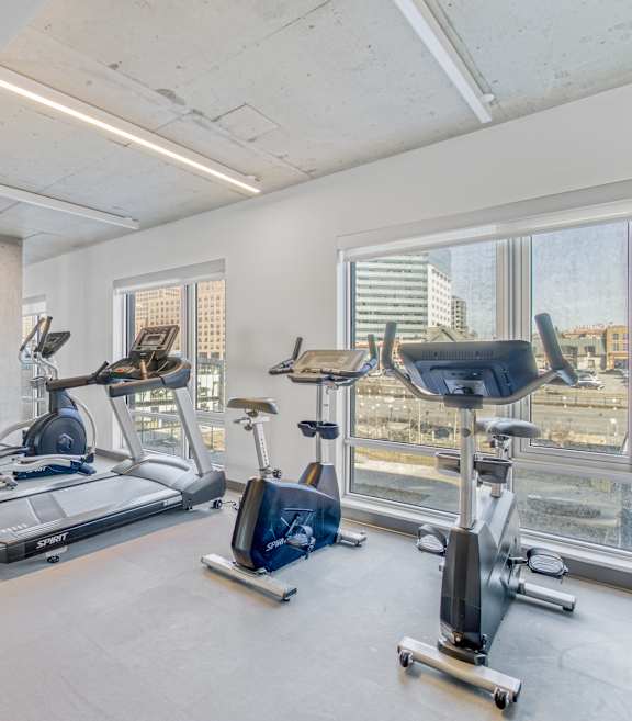 A spacious gym with a variety of exercise equipment and a view of the city skyline.