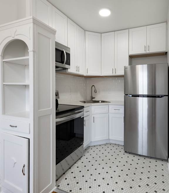 A kitchen with white cabinets and a silver refrigerator.