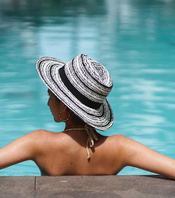 A woman in a striped hat is sitting by a pool.