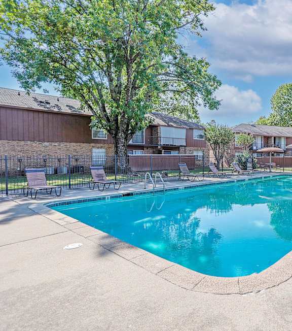 A swimming pool surrounded by lounge chairs and trees.