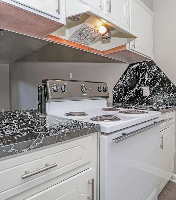 A kitchen with a white stove top oven and a marble counter top.