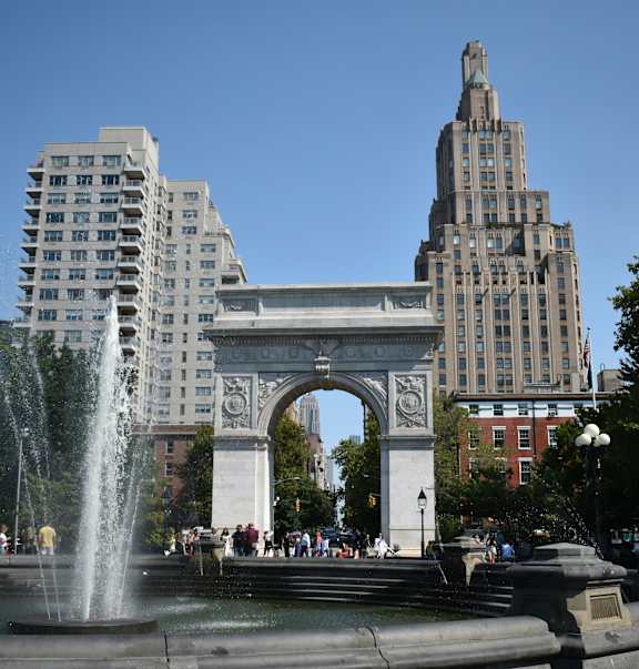 A fountain in front of a large archway and buildings.