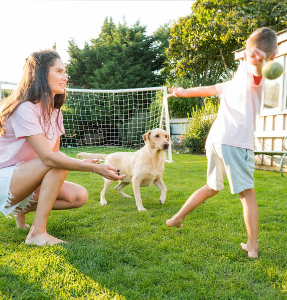 A woman and a child are playing with a dog in a backyard.