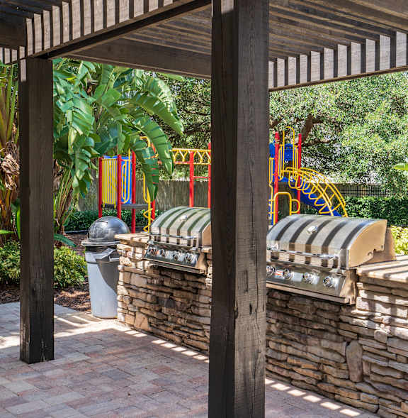 a pergola with a stone wall and a playground in the background