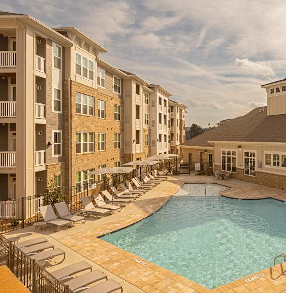 A large swimming pool surrounded by lounge chairs and apartment buildings.