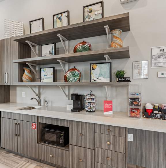 A kitchen with a refrigerator, microwave, and shelves with various items.