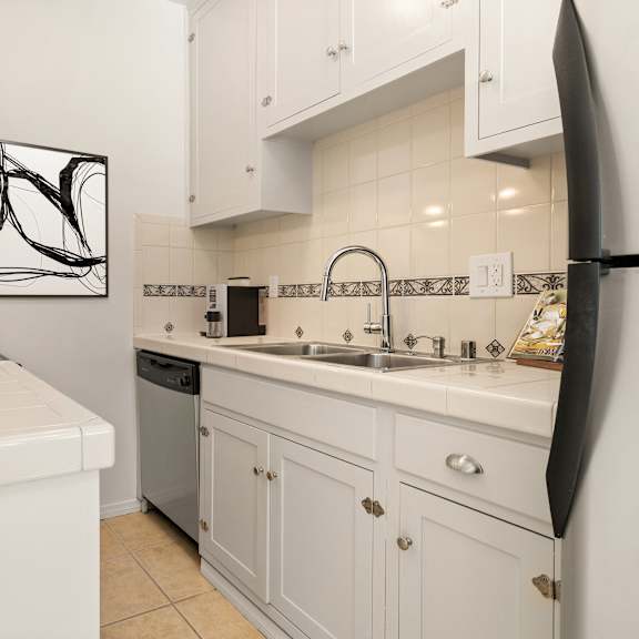 A white kitchen with a black fridge and a black and white picture on the wall.