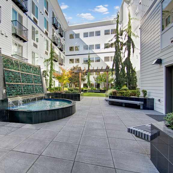 The courtyard with a beautiful cascading waterfall with a small pool in front of trees, plants, and a pathway to the green space at the Artiste Apartment Homes.