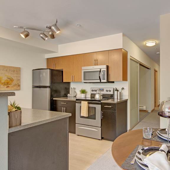 A kitchen with stainless steel appliances, marble countertops, and large wooden cabinets at Leilani Apartment Homes. 