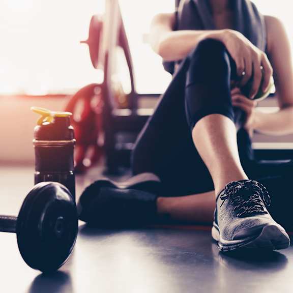 A woman is sitting on the floor with a dumbbell and a bottle of water in front of her.