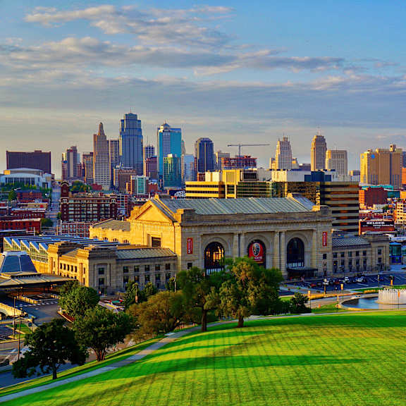 A city skyline at sunset with a large arch structure in the foreground.