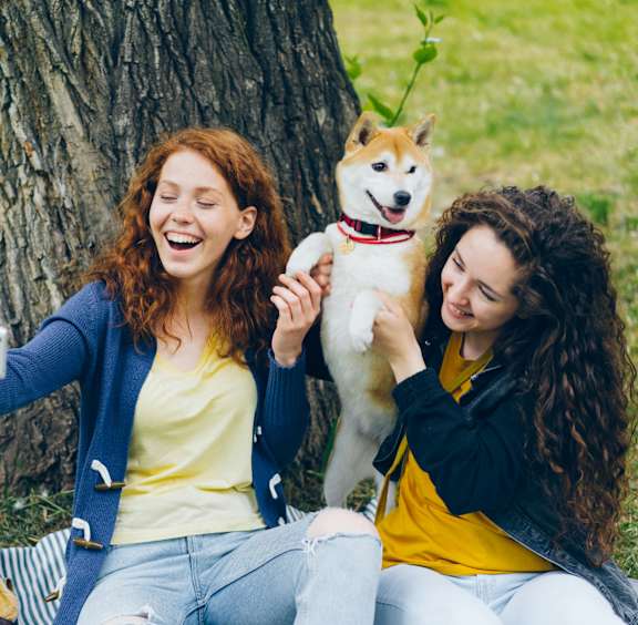 two women sitting under a tree with a dog
