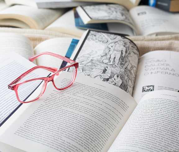 Red glasses resting on an open book on a tabletop, creating a calm reading moment.