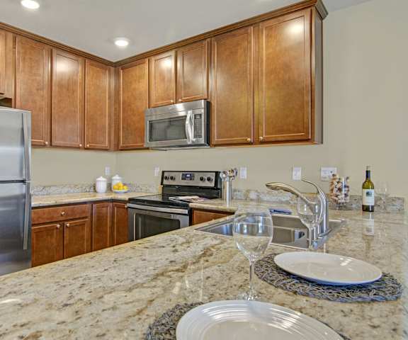 A large kitchen with a table place set with plates and wine glasses, as well as stainless steel appliances, spacious marble countertops, and large wooden cabinets at Ondine at Juanita Bay Apartments. 
